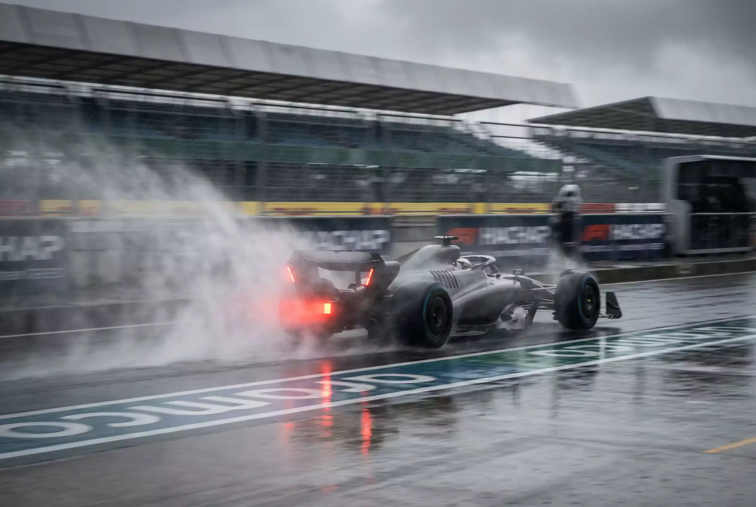 Formel-1-Wagen fährt bei Regen mit Spritzwasser auf nasser Strecke